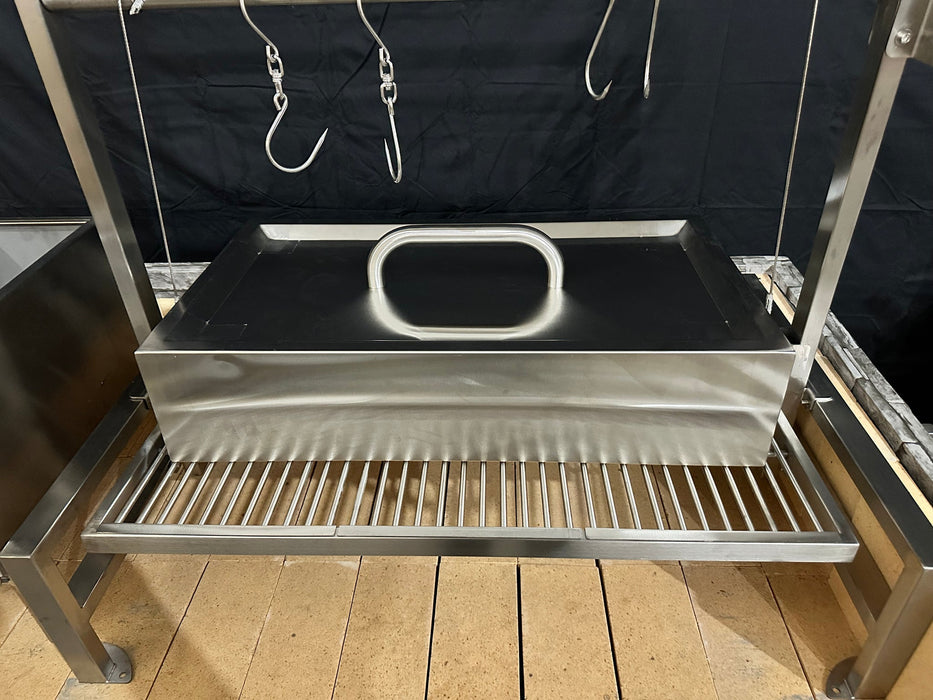 Stono Outdoor Living The Tagwood BBQ Large Top Lid - BBQ59SS by Tagwood BBQ features a stainless steel smoker or roasting box with a spacious lid and handle, placed on a slatted metal rack with hanging hooks above, all set against a black backdrop.