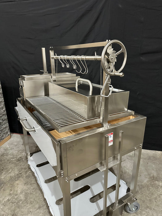 Stono Outdoor Living The Tagwood BBQ Large Top Lid - BBQ59SS by Tagwood BBQ is a stainless steel outdoor grill featuring a spacious grate, side tray, hanging hooks, hand crank, storage compartments, and large top lid for oven-style cooking—shown on a concrete floor with a black backdrop.