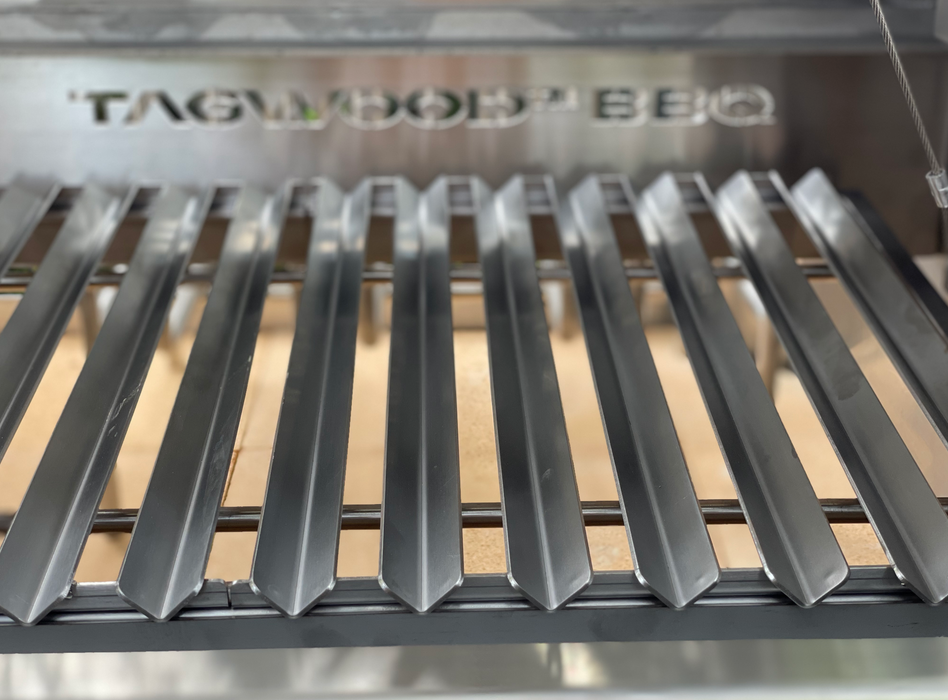 Stono Outdoor Living Close-up of a clean, empty Tagwood BBQ V-Shape Grate for BBQ09SS - BBQ97SS, made of 304 stainless steel with V-shaped bars. The Tagwood BBQ brand name is visible in the background as part of a barbecue grill accessory.