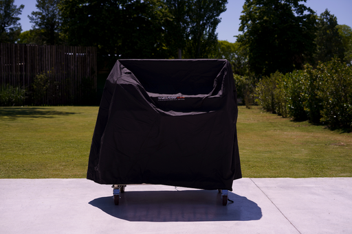 Stono Outdoor Living A Tagwood BBQ Grill Cover for BBQ23SS Grill - BBQ86SS by Tagwood BBQ sits on a wheeled grill on a concrete patio, with green grass and trees behind it on a sunny day.