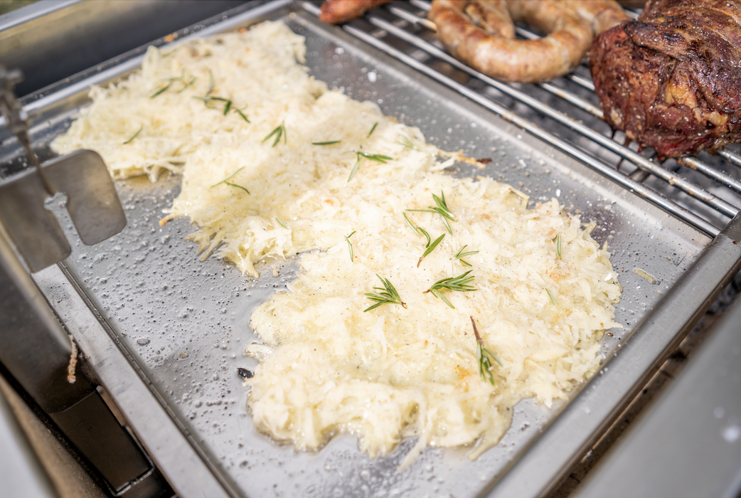 Stono Outdoor Living Shredded potatoes with rosemary cook on the Tagwood BBQ Interchangeable Griddle for BBQ03SS/05SS - BBQ58SS, alongside sausages and roasted meat, making a delicious feast across the grilling surface.