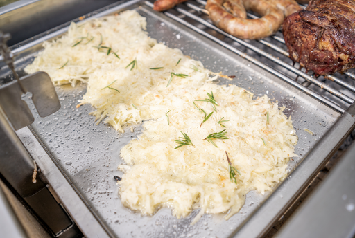 Stono Outdoor Living Shredded potatoes with rosemary cook on the Tagwood BBQ Interchangeable Griddle for BBQ03SS/05SS - BBQ58SS, alongside sausages and roasted meat, making a delicious feast across the grilling surface.
