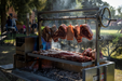 Stono Outdoor Living Large cuts of raw meat hang from Tagwood BBQ S Shape Meat Hooks (set of 7, BBQ56SS) above a 304 stainless steel grill, with more meat slow cooking over hot coals as smoke rises from the outdoor barbecue in a park.