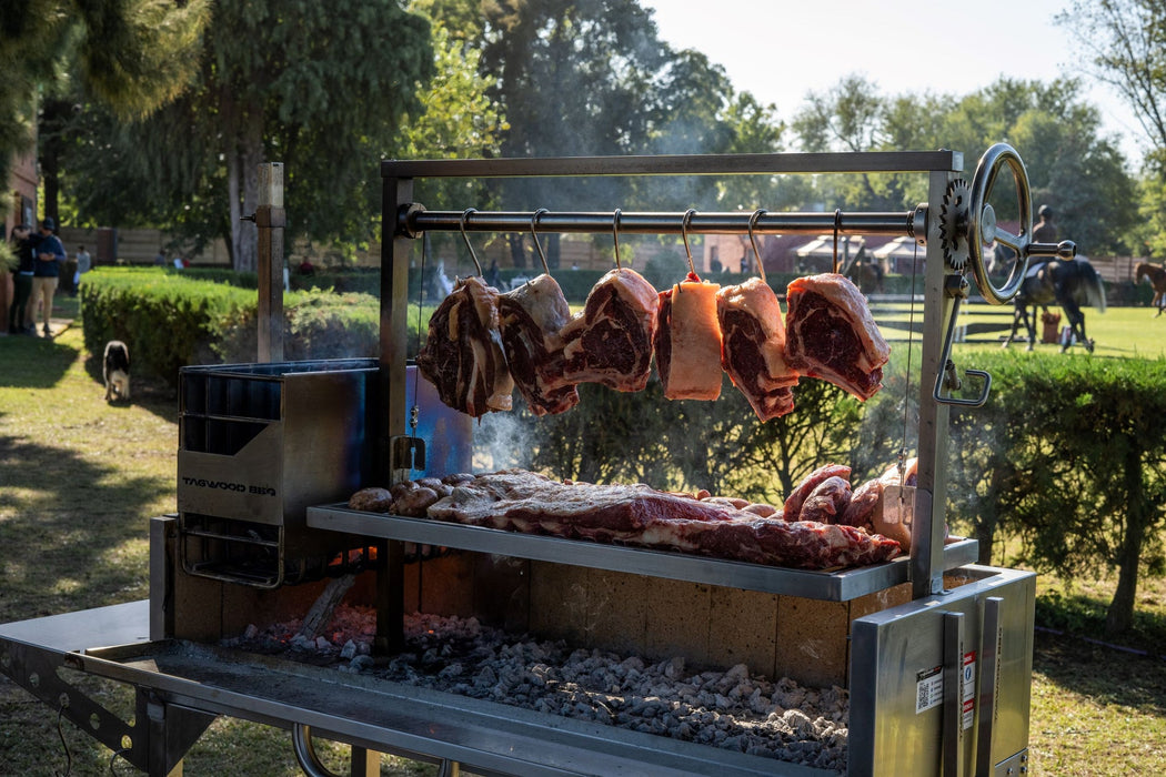 Stono Outdoor Living Several large cuts of meat are slow cooking outdoors on a 304 stainless steel grill, suspended with Tagwood BBQ S Shape Meat Hooks (set of 7) - BBQ56SS, by Tagwood BBQ, with trees, grass, and people visible on a sunny day.