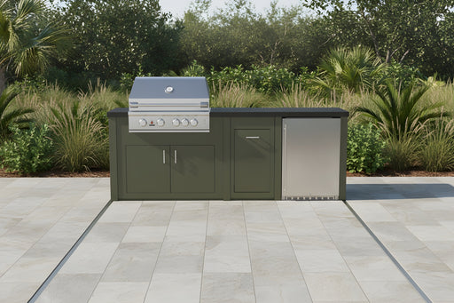 Stono Outdoor Living The Sullivan - 98" Outdoor Kitchen Island by Stono Outdoor Living features a green island, stainless steel grill, sink, and mini fridge on a tiled patio surrounded by lush greenery and trees.