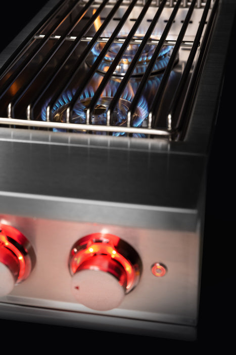 Stono Outdoor Living Close-up of the TrueFlame Double Side Burner - TFSB2 by TrueFlame in an outdoor kitchen, with blue flames beneath the grate and two red-lit control knobs, highlighting its high BTU performance for powerful cooking.