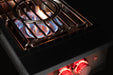Stono Outdoor Living A close-up of the TrueFlame Natural Gas Power Burner (TFPB) shows blue flames beneath metal grates. Two red-lit knobs on the black panel highlight this high BTU model by TrueFlame—ideal for any outdoor kitchen against a black background.