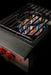 Stono Outdoor Living A close-up of the TrueFlame Propane Gas Power Burner - TFPBL by TrueFlame, featuring blue and orange flames, black grates, two red knobs, and high BTU output—ideal for outdoor kitchens—set against a sleek black background.