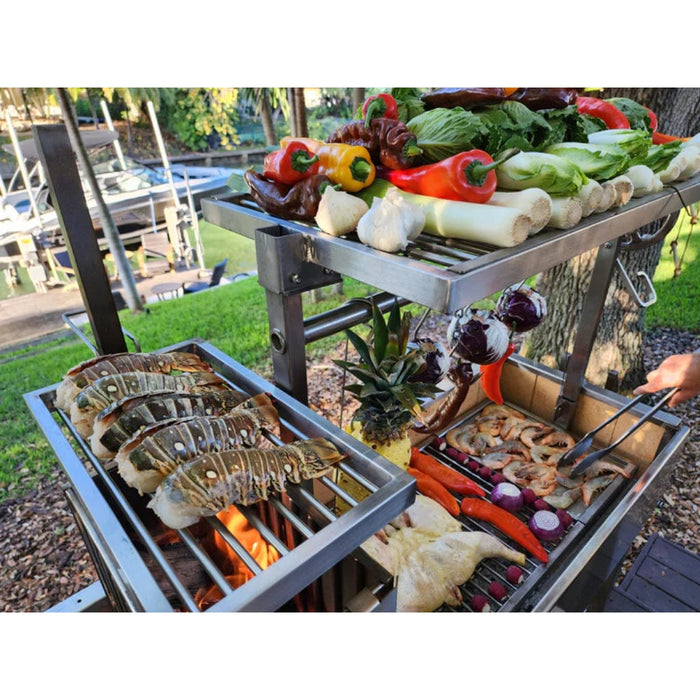 Stono Outdoor Living Colorful vegetables, herbs, and lobster tails are being grilled outdoors on the Tagwood BBQ Argentine Santa Maria Wood Fire & Charcoal Grill - BBQ06SS by Tagwood BBQ near a lakeside dock, surrounded by grass and trees.