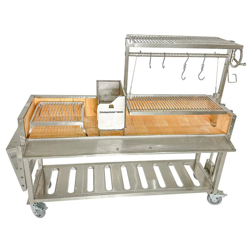 Stono Outdoor Living The Tagwood BBQ Argentine Santa Maria Wood Fire & Charcoal Grill (BBQ06SS) by Tagwood BBQ features 304 stainless steel, multiple grilling racks, food hooks, a wooden workspace, storage shelf, and wheels for easy mobility.