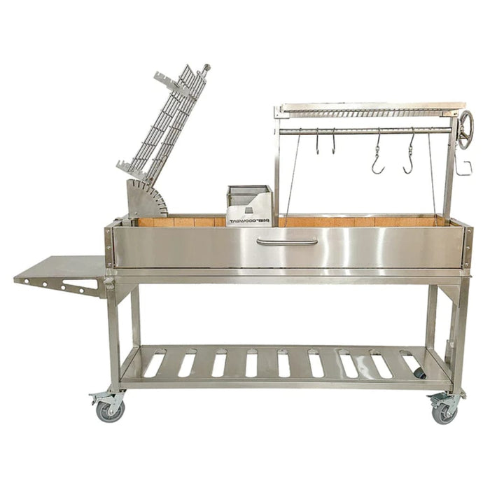Stono Outdoor Living The Tagwood BBQ Argentine Santa Maria Wood Fire & Charcoal Grill (BBQ06SS) by Tagwood BBQ features 304 stainless steel, a side shelf, hanging hooks, grilling racks, wheels, a storage shelf below, and an Argentine-style cooking area with a partially open lid.