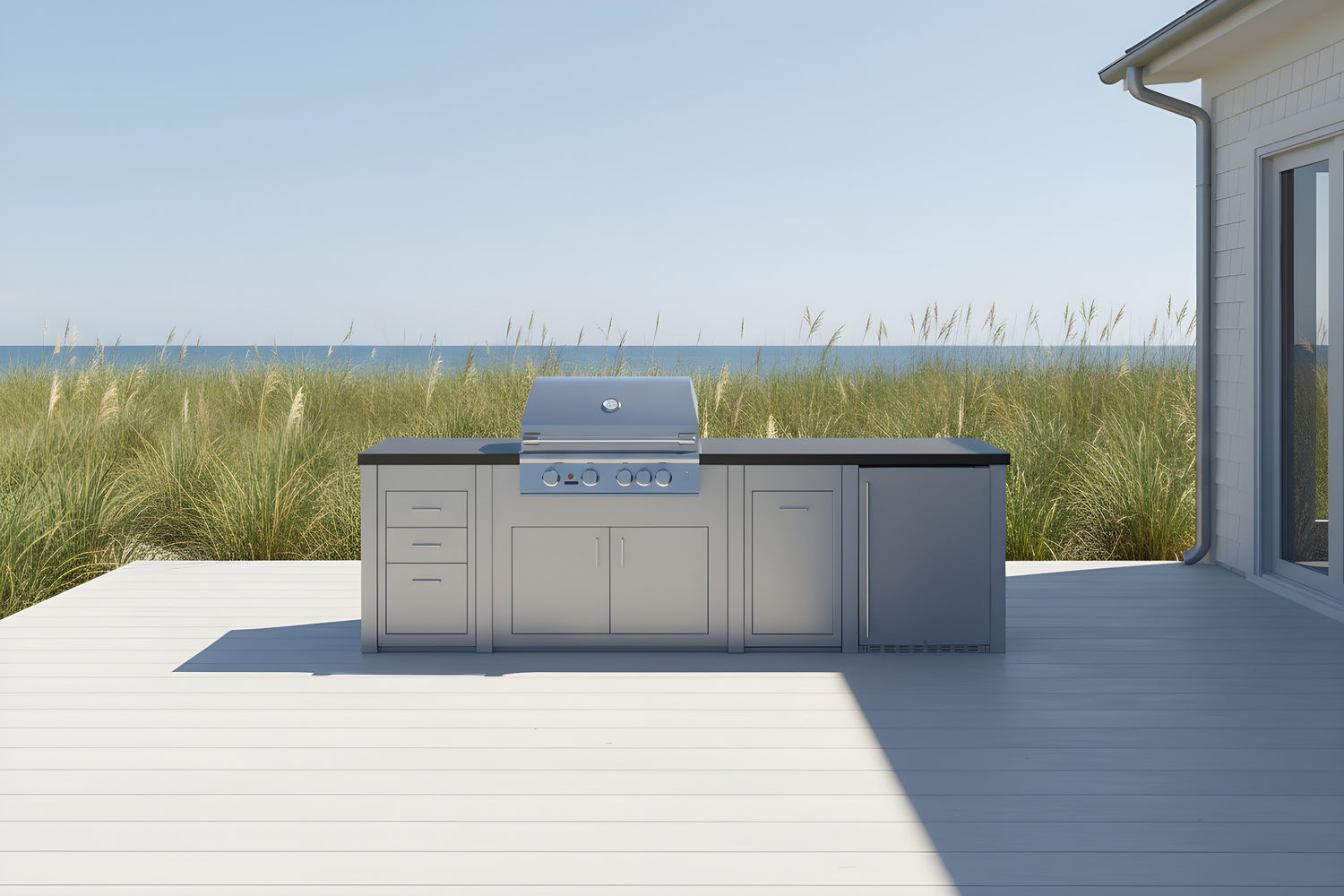 Stono Outdoor Living A modern outdoor kitchen with a built-in grill and storage cabinets sits on a light gray patio, overlooking tall grass and the ocean under a clear blue sky.