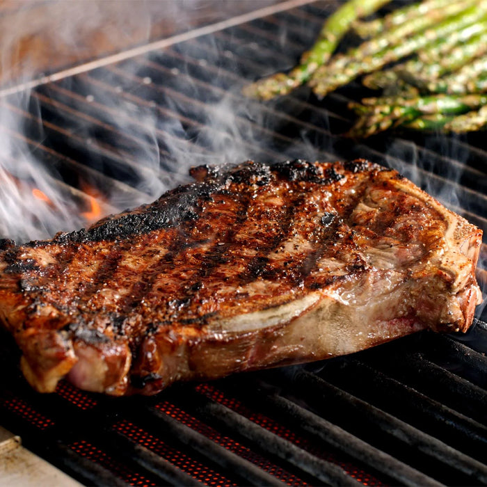 Stono Outdoor Living A thick, juicy steak sizzles on a Blaze Grills Infrared Searing Burner (BLZ-IRN), made for Blaze and Blaze LTE grills, as smoke rises and asparagus spears roast nearby.