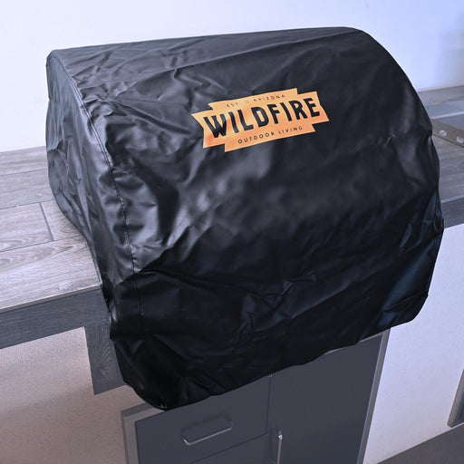 Stono Outdoor Living The Wildfire Outdoor Living 42" Vinyl Grill Cover (WFGC42) in black with a bold orange Wildfire logo protects a barbecue grill on a gray outdoor kitchen countertop.