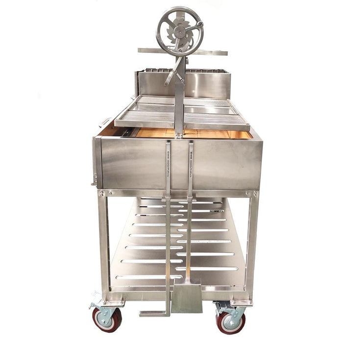 Stono Outdoor Living The Tagwood BBQ XL Double Argentine Santa Maria Wood Fire & Charcoal Grill (BBQ24SS) by Tagwood BBQ features 304 stainless steel, a hand-crank wheel, open fire grilling surface, lower storage rack, and durable rectangular design with wheels shown front-facing.
