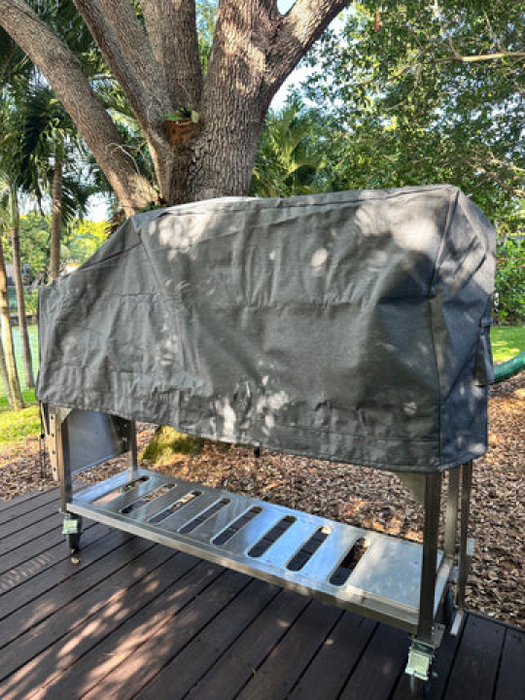 Stono Outdoor Living A Tagwood BBQ outdoors metal grill, protected by the Tagwood BBQ BBQ08SS Cover - COVE08, stands on a wooden deck beneath a large tree amid greenery and sunlight.