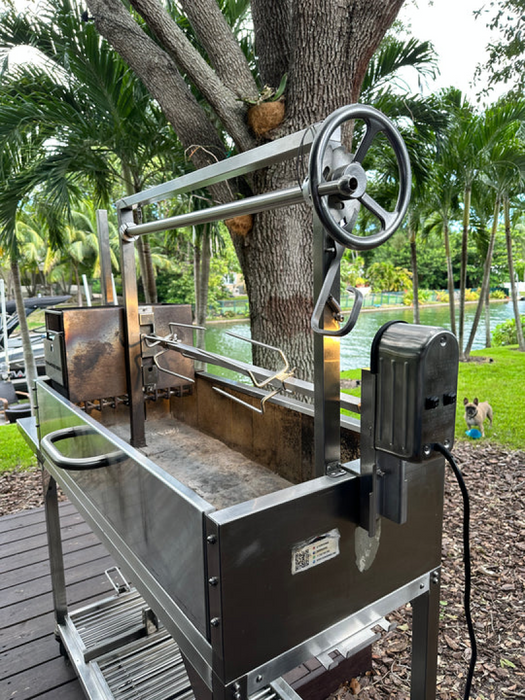 Stono Outdoor Living The Tagwood BBQ Stainless Steel Rotisserie Kit - BBQ50SS PRO by Tagwood BBQ is set up on a deck near trees and a canal, with a wheel, electric motor, lush greenery in the background, and a dog visible.