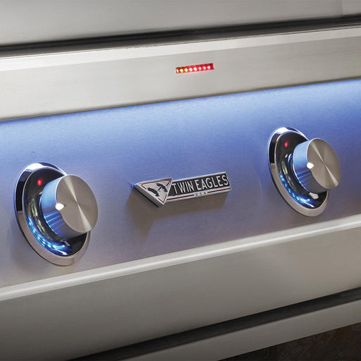 Stono Outdoor Living Close-up of the Twin Eagles Eagle One 54-Inch 4-Burner Built-In Propane Gas Grill (TE1BQ54RS-L), showing two round control knobs with blue-lit temperature controls, the Twin Eagles logo between them, and a red LED display above the logo.