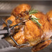 Stono Outdoor Living A golden-brown roasted chicken is cooked on the Delta Heat 38-Inch 3-Burner Built-In Natural Gas Grill with Sear Zone & Infrared Rotisserie Burner (DHBQ38RS-DN), garnished with fresh rosemary sprigs.