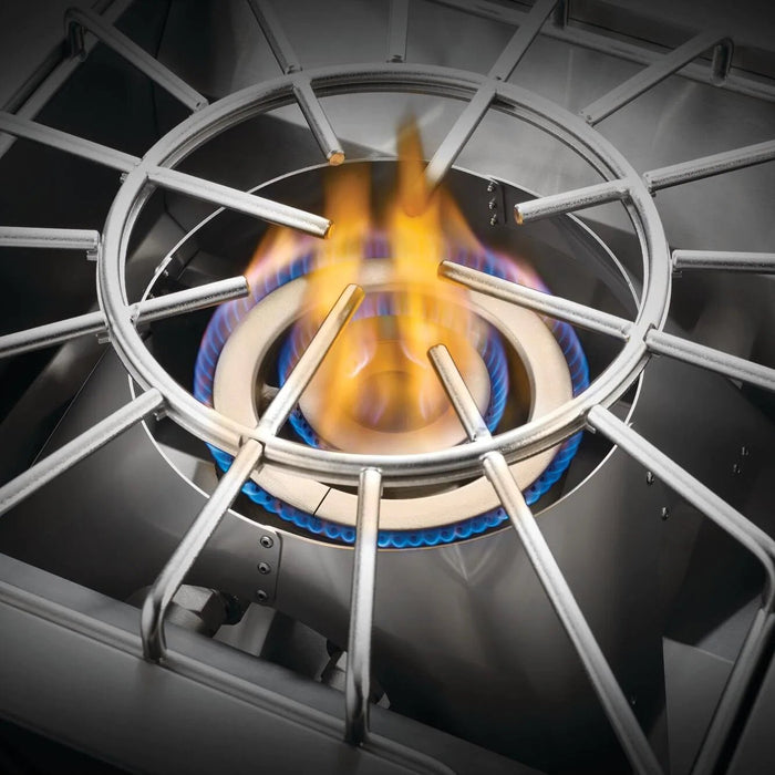 Stono Outdoor Living Close-up of the Napoleon Built-In 700 Series Propane Gas Power Burner (BIB18PBPSS) with blue and yellow flames visible under a metal grate, indicating the burner is on; includes stainless steel cover.