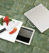 Stono Outdoor Living A kitchen floor features the Delta Heat Trash Chute - DHTC by Delta Heat. Its open lid reveals storage beneath, while a removable cutting board above holds sliced tomatoes, a knife, and chili peppers.